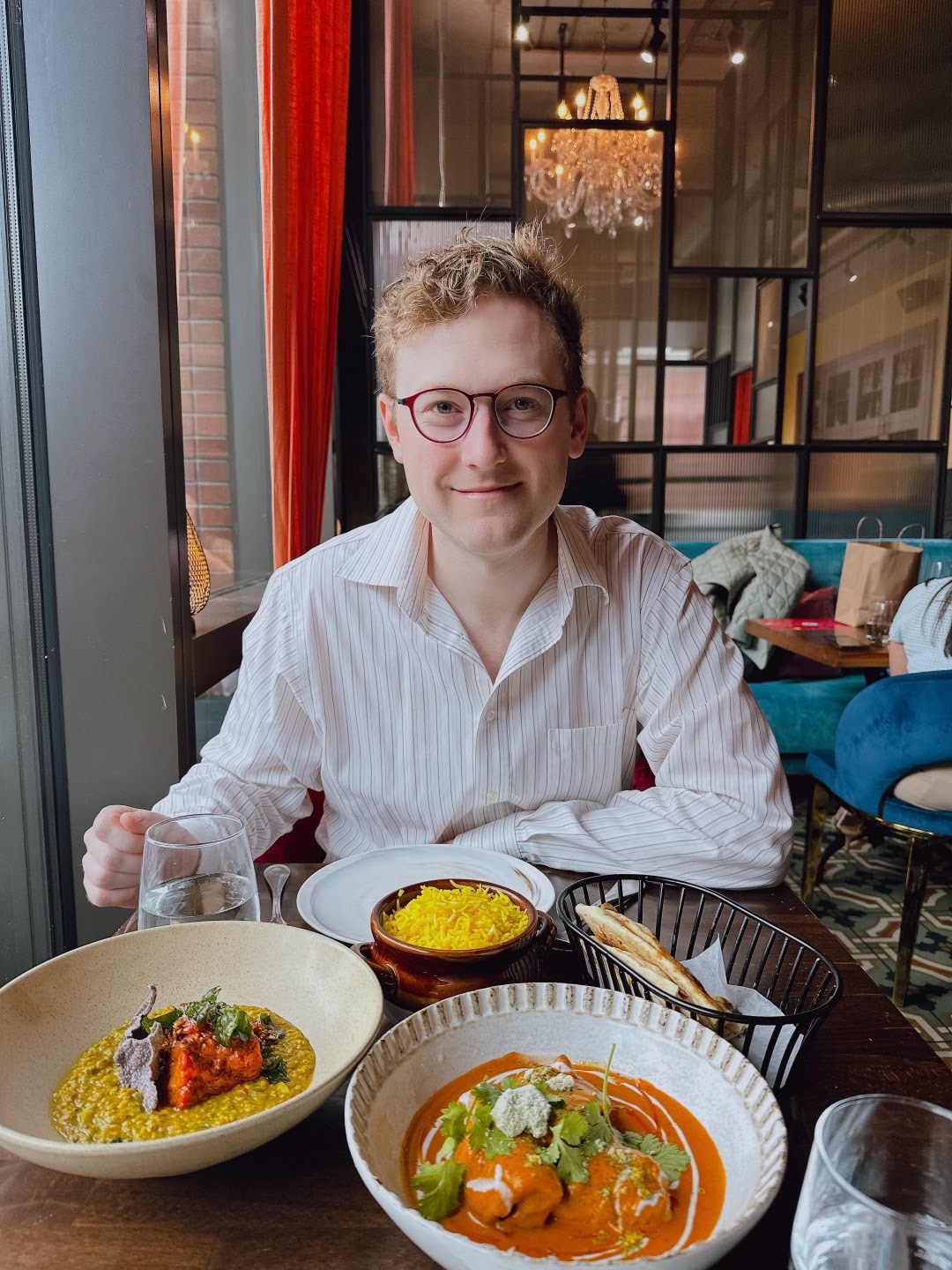 Smiling at a restaurant table spread with Indian food